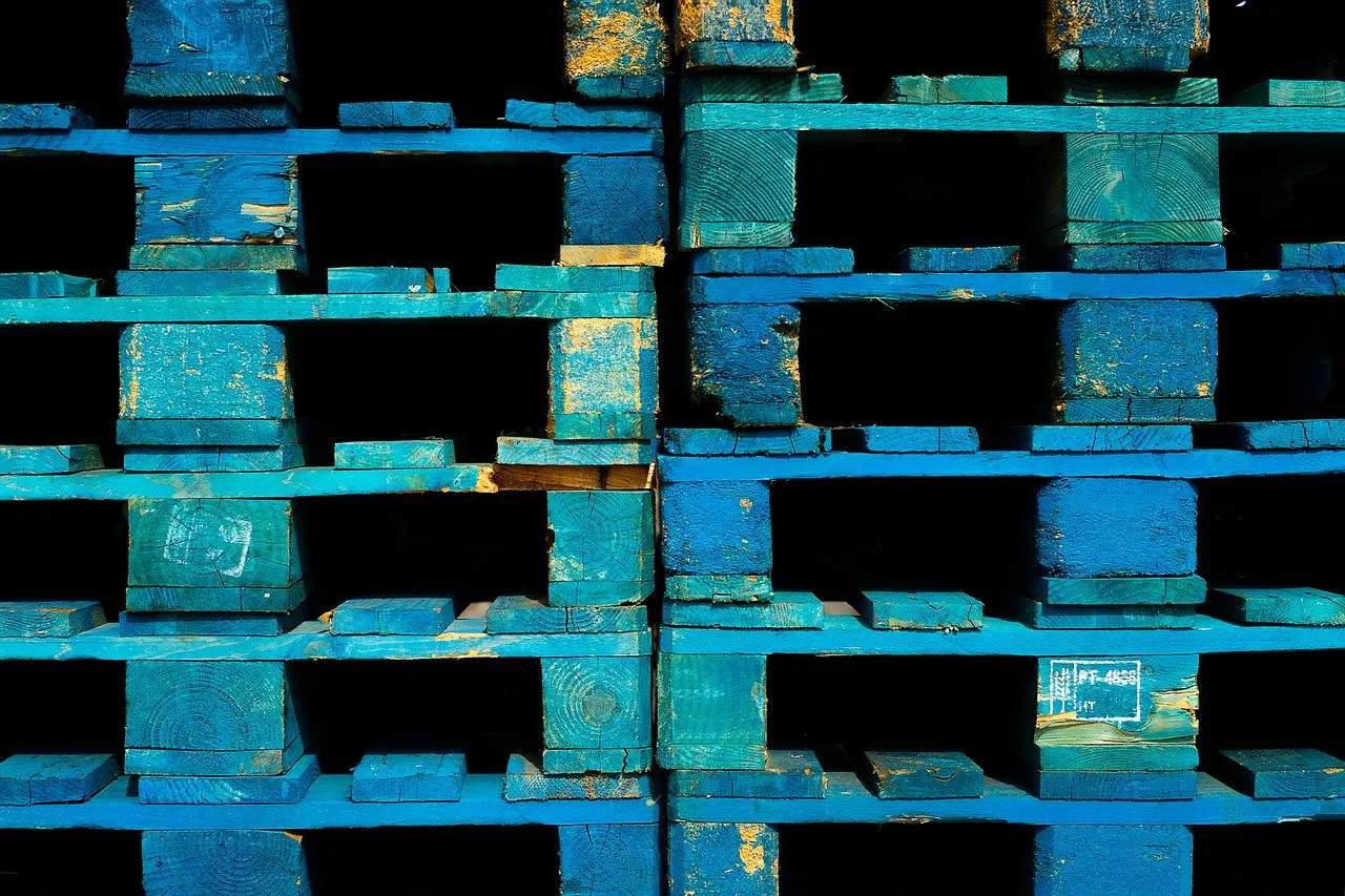Stapel blau lackierter Holzpaletten, teils mit Kennzeichnung, dicht nebeneinander aufgeschichtet.