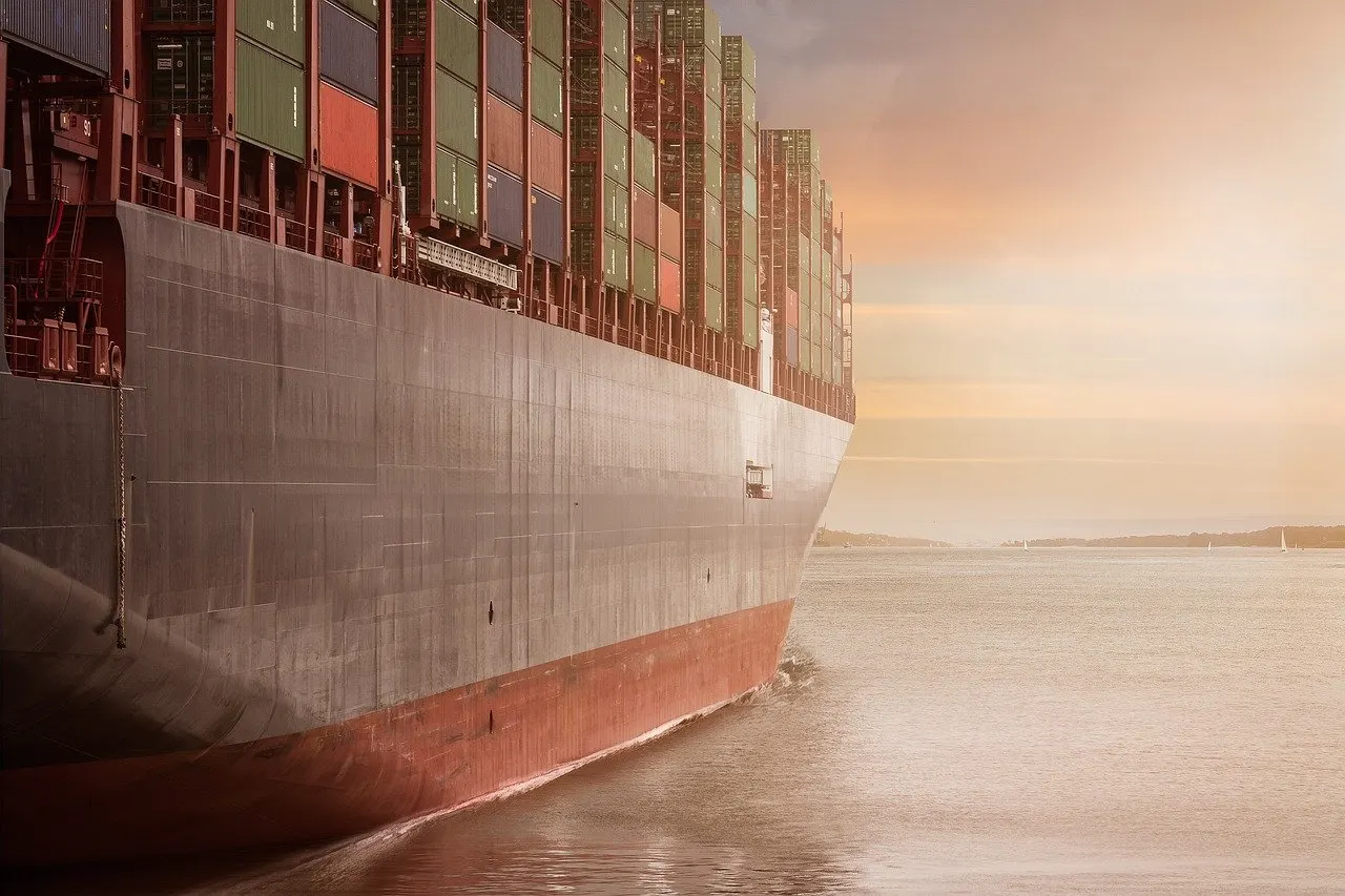 Großes Containerschiff mit hoch gestapelter Ladung fährt bei Sonnenuntergang auf ruhigem Wasser.
