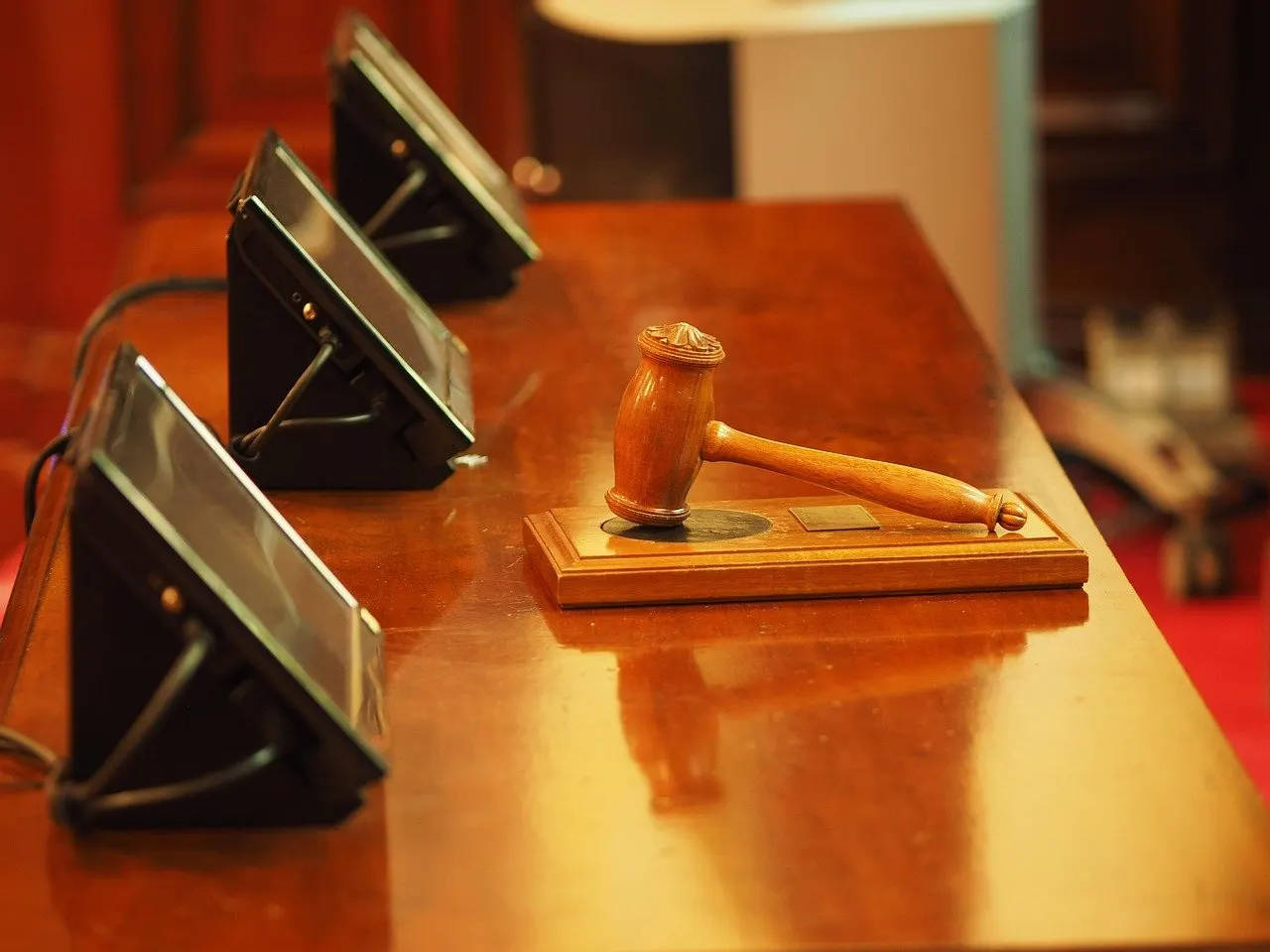Holzhammer auf Sockel in einem Gerichtssaal mit Monitoren im Hintergrund