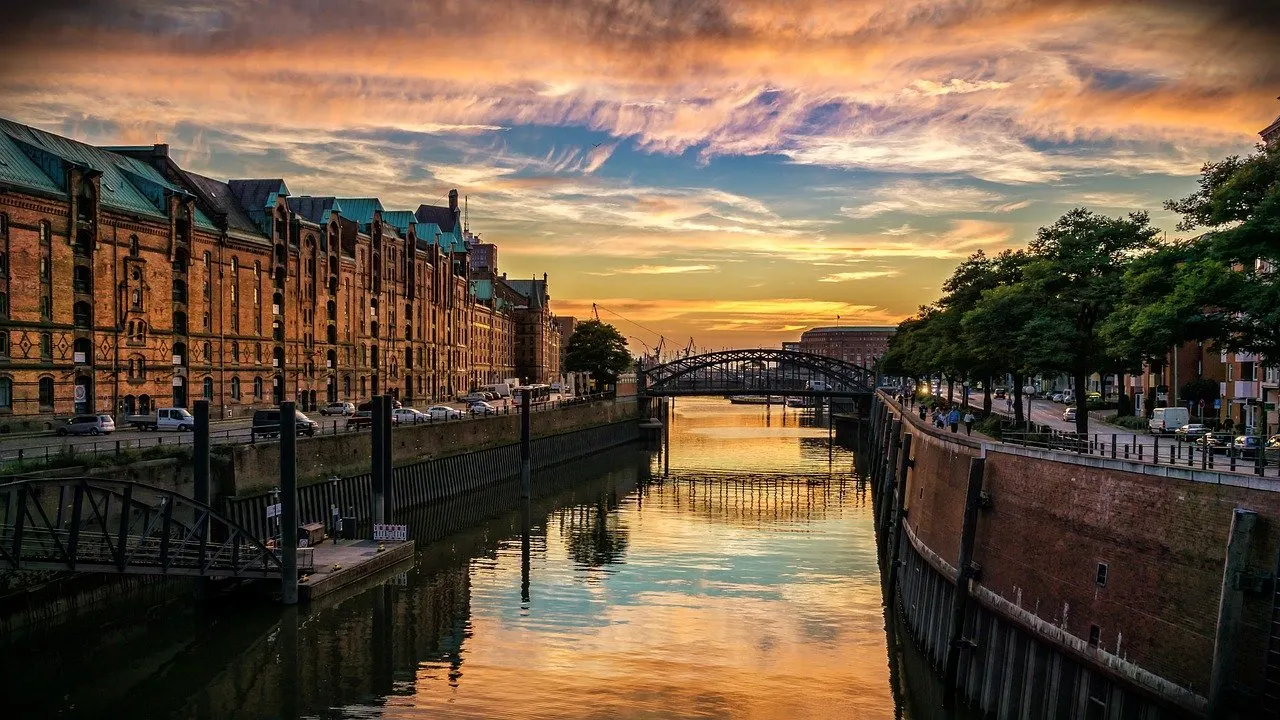 Backsteinspeicher am Kanal bei Sonnenuntergang, Brücke und Bäume am Wasser.