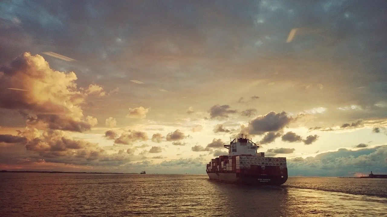 Containerschiff auf ruhigem Meer bei Sonnenuntergang unter bewölktem Himmel